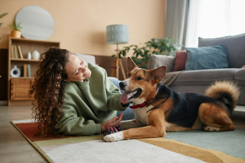 Happy Girl Playing with Dog Lying on Floor in Home