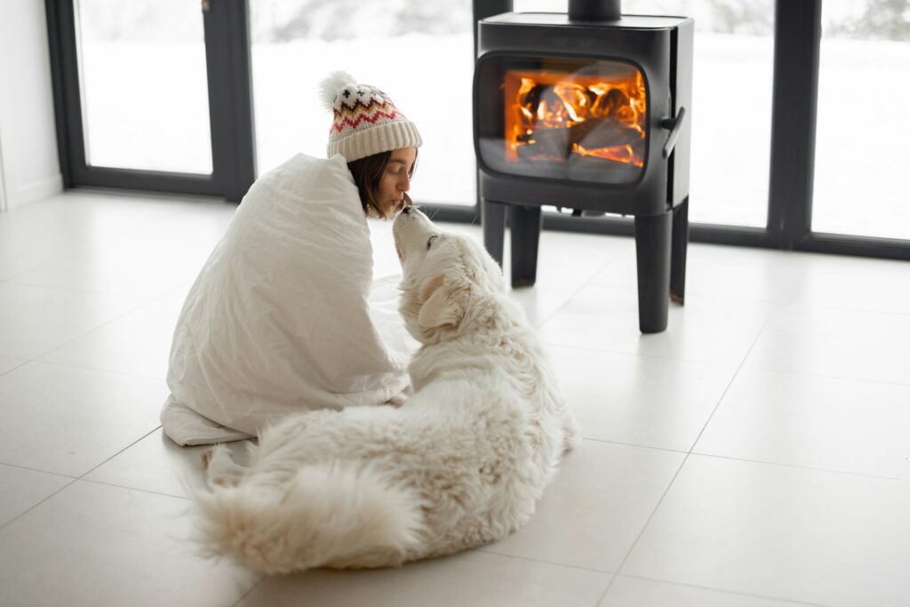 Woman with dog at home with burning fireplace during wintertime
